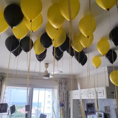 Black and yellow helium balloons with photos attached to the ribbons, floating on the ceiling. This is a great way to personalize a surprise.