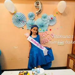 The birthday girl looking beautiful in her blue dress, standing by her balloon-themed cake.