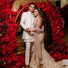 A vision in red and gold. Amy and Joe are framed by a stunning arch of red roses, creating a luxurious and romantic portrait that was a highlight of their wedding reception.