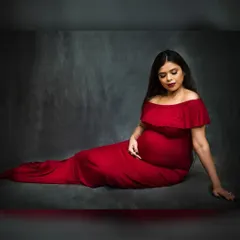 A simple yet powerful seated portrait against a textured dark grey backdrop. The focus here is entirely on the mother-to-be, with the vibrant red of the gown providing a beautiful contrast.