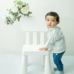 Capturing the 'just about to walk' phase. This toddler holds onto the chair for support, a perfect way to document this significant milestone in a clean and modern style.