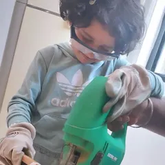 Fully kitted out with gloves and safety glasses, this young builder is learning the fundamentals of woodworking. We believe in teaching real skills in a completely safe setting.