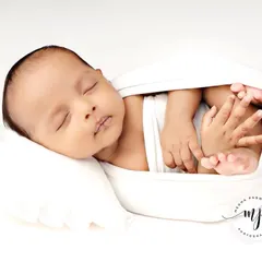 A full-body shot of the baby in the white 'potato sack' pose, looking like they are floating on a cloud.