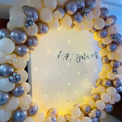 A full circular balloon arch in cream and metallic silver, with fairy lights in the background for a soft, celebratory glow.