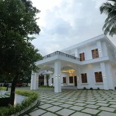 A view of a modern white villa where our landscaping provides a clean, structured look. The design features a geometric paver driveway with grass joints, neat garden beds, and mature trees that frame the home's impressive facade.