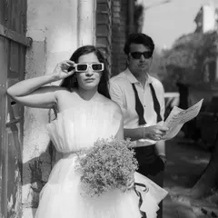 A cool, editorial-style black and white shot. Her quirky sunglasses and his classic look create a fun contrast, making this feel like a behind-the-scenes photo from a fashion magazine shoot.