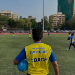 A view from behind a coach in a yellow bib, watching over his players during a training session. This perspective highlights the focus, heart, and potential our coaches see on the field every day.