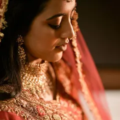 A quiet, contemplative bridal portrait. The warm lighting highlights the rich details of her jewelry and the delicate embroidery of her wedding outfit.