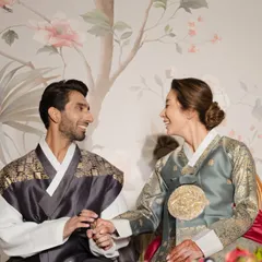 A candid shot of the couple sharing a happy moment during their Paebaek ceremony, seated in front of a custom-designed backdrop with a traditional Korean floral painting.