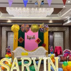 For baby Sarvin's first Lohri, I created this personalized stage featuring large, illuminated letters of his name. The setup includes a comfortable sofa for the family, colorful drapes, and festive Punjabi elements like decorative umbrellas.