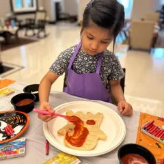 The perfect pizza starts with the perfect sauce. I show the kids how to spread the tomato sauce evenly on their ghost-shaped pizza dough before adding cheese and toppings.