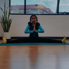Charvi in a seated wide-legged forward bend with hands in prayer. Her focus and dedication are evident in every pose she practices.
