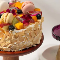 A side view of my Almond & Fruit Cake, showing the crunchy toasted almonds covering the sides and the abundance of fresh fruit and macarons on top.