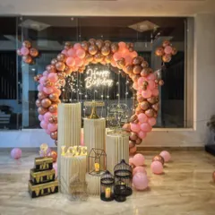This rose gold and pink balloon ring arch is one of my most popular designs for elegant birthdays. The setup includes a full set of white cylindrical stands and decorative props like bird cages and a lit-up tree.