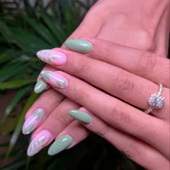 When elegance meets nature. This beautiful almond-shaped set combines solid pastel green nails with accent nails featuring a pink base and delicate white leaf patterns.