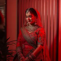 A stunning bridal portrait using dramatic red lighting to create a bold, cinematic feel. This shot highlights the bride's serene expression and the intricate details of her red lehenga and jewelry.