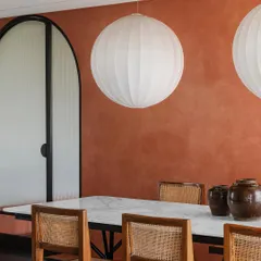 A closer look at the dining area, where large spherical fabric lights float above the marble table. The warm terracotta wall and cane chairs create a welcoming environment for gathering.