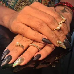 A dramatic set of long stiletto nails with a mix of black glitter and holographic gold flake accents.