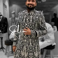 A client looking happy in a black sherwani-style kurta with all-over white floral embroidery. The dense pattern gives the garment a rich, textured look that's perfect for a festive occasion.