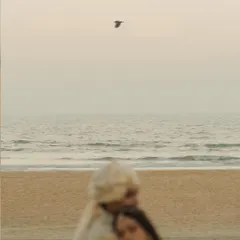 An artistic, blurred shot of a couple embracing on a quiet Goa beach at dusk, with a single bird flying overhead. This frame feels like a soft, still, and infinite memory from a beach pre-wedding session.