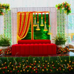 This Haldi or Mehendi backdrop is full of life, featuring a bright red sofa against a backdrop of marigold curtains and a modern white lattice frame. It's a perfect blend of traditional and contemporary design.