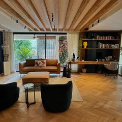 An intimate yet open study space designed for comfort and focus. The room features warm herringbone wood floors and exposed ceiling beams, complemented by a rich navy blue accent wall. A mix of leather and fabric seating creates a relaxed atmosphere, perfect for reading or working from home.