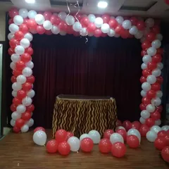 A spiral red and white balloon arch on a stage, creating a focal point for a cake-cutting ceremony or performance area.