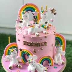 A truly magical unicorn cake, covered in pink buttercream and adorned with a whole family of cute, playful unicorns and rainbows.