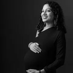 A classic black and white maternity portrait against a dark background. The lighting is carefully shaped to highlight the mother's features and her beautiful pregnancy glow.