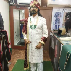 We design complete, head-to-toe groom ensembles. This client is ready for his wedding day in a custom white sherwani, complemented by a matching pagri (turban), a contrasting maroon dupatta, and traditional jewelry for a cohesive, royal look.