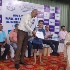 A proud moment as our student receives his trophy and certificate on stage at the Yonex-Sunrise Karnataka State Ranking Badminton Tournament.
