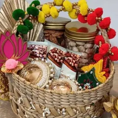 A vibrant and traditional Diwali hamper basket. It's overflowing with goodies, including jars of dry fruits, snacks, and beautiful pearl-decorated 'shubh-labh' hangings.