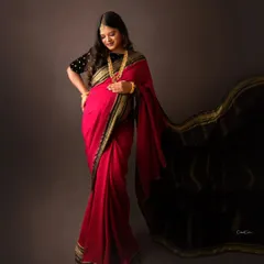 A graceful pose showcasing the beautiful drape of this red and black saree. The mom-to-be looks down at her bump with a gentle smile.