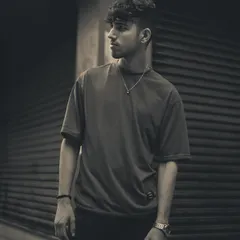 A moody, sepia-toned black and white portrait of a male subject. The urban background and strong pose create a classic, masculine image with a timeless quality.