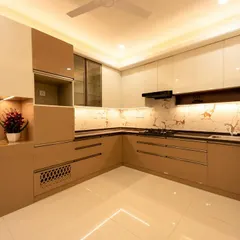 A beautiful and functional L-shaped kitchen in beige and brown tones. The design includes ample storage, under-cabinet lighting for task areas, and a stunning marble-patterned backsplash that adds a touch of luxury.