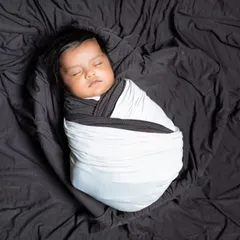 A minimalist newborn shot, with the baby swaddled in black and white on a simple black background.
