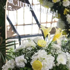 A close up of the "Citrus Got Real" mirror decor. The reflection shows the bright and airy venue, while the foreground highlights the fresh yellow lilies, white carnations, and lemon slice accents.