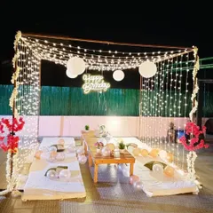 A cozy and magical terrace party setup, creating a cabana with a canopy of fairy lights, low seating, and a "Happy Birthday" neon sign for a unique celebration under the stars.