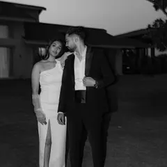 A chic and moody black and white portrait. The couple's formal attire and the subtle, knowing glance they share create a sophisticated and timeless image with a touch of old-world glamour.