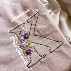 A custom-made initial 'K' filled with delicate purple and white flowers on a pink sweatshirt. This is a perfect example of my floral embroidery work.