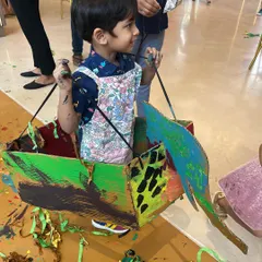 A young boy stands inside a colorful boat he painted himself. This is a perfect example of how our art projects often become props for imaginative play and adventure.