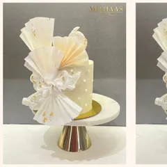 A white celebration cake featuring intricate, fan-like rice paper sails and delicate pearl details. The design is finished with flecks of 24-carat gold, creating a piece that is both modern and timelessly elegant.
