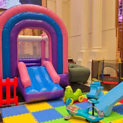 A colorful and safe play area for kids, with a rainbow bouncy castle, soft mat flooring, and various toys.