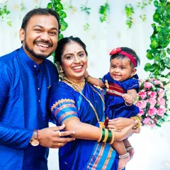 A happy family of three, dressed in matching blue traditional outfits, smiles for a portrait at a Naming Ceremony.