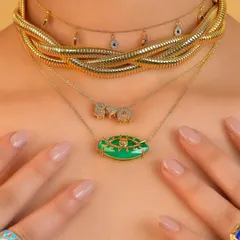 A close-up of a summer-ready necklace stack. I love the combination of the chunky snake chain, the delicate evil eye choker, the initial necklace, and the bold green pendant.