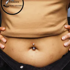 A classic navel piercing featuring a simple, elegant crystal barbell. This close-up shows the clean placement and precision I aim for with every body piercing.