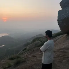 A trekker stands with arms crossed, taking in the serene sunrise view from the top of Uttari Betta.