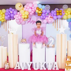A full-length portrait of the birthday girl seated proudly amidst her party decorations.
