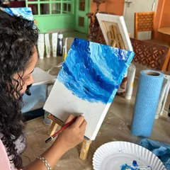 A close-up of the painting process. Here, a participant uses a brush to define the waves in her beautiful landscape painting.