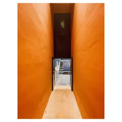 A narrow, compressed passageway with vibrant orange walls opens into a larger space, creating a dramatic sense of arrival. I use such spatial sequences to guide movement and shape the emotional experience of moving through a building.